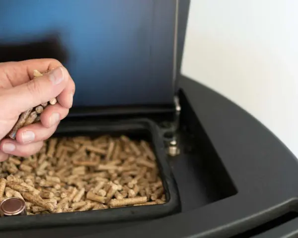 Mano cargando pellets en una estufa de pellets. Preparando la instalación de la estufa de pellets para un invierno cálido.