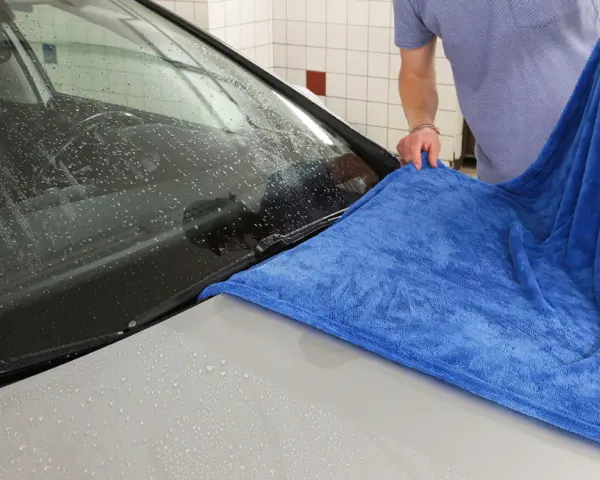 En person torkar av en bilruta med en blå torkhandduk.