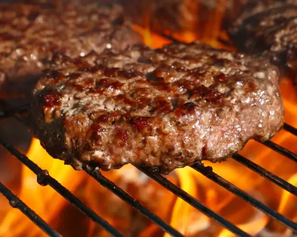 Soczyste kotlety wołowe smażące się na grillu z płomieniami.