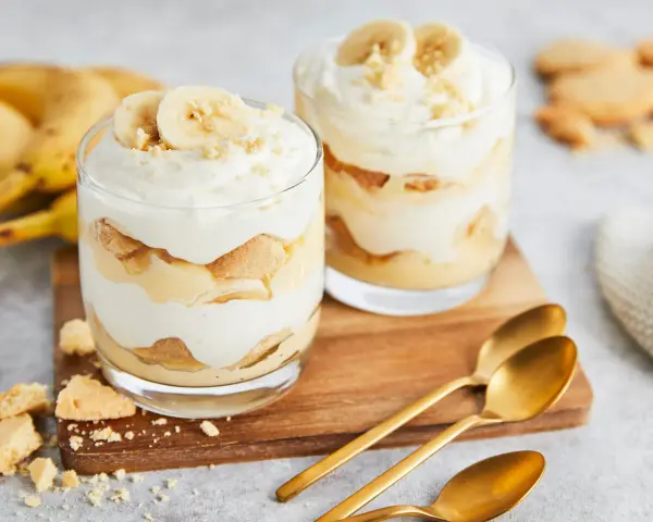 Zwei Gläser mit cremigem Bananenpudding, geschichtet mit Keksen und Bananenscheiben. Ein köstliches Bananenpudding Rezept zum Nachmachen.