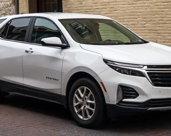 Biały Chevrolet Equinox, wszechstronny chevrolet suv, zaparkowany na brukowanej ulicy przed ceglanym budynkiem.