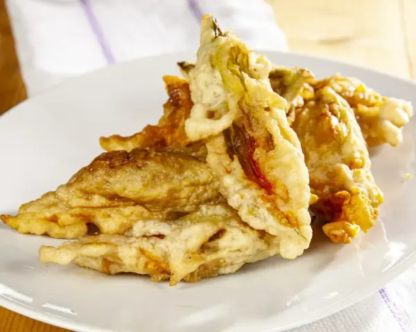 Fiori di zucca fritti dorati e croccanti su un piatto bianco, pronti per essere gustati.