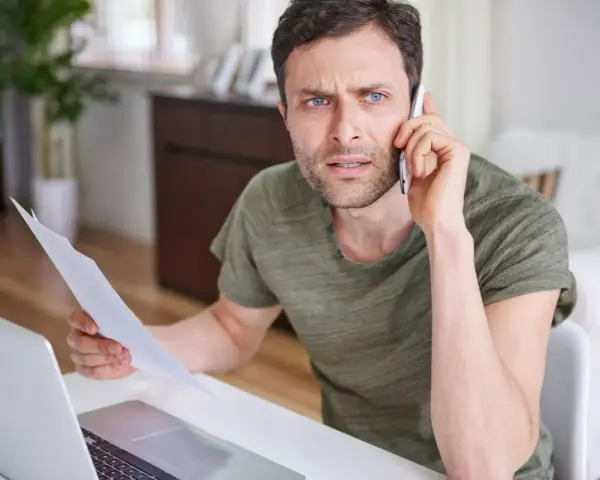 Zmartwiony mężczyzna z dokumentami w ręku rozmawia przez telefon, martwiąc się o niespłacony kredyt odnawialny.