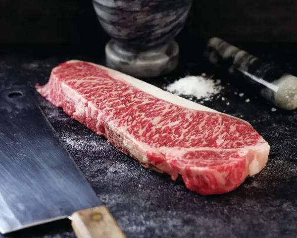 Wyjątkowy stek z krowy wagyu, gotowy do przygotowania. Obok nóż i moździerz z solą.