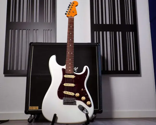 Weiße E-Gitarre mit sechs Saiten steht vor einem Verstärker.