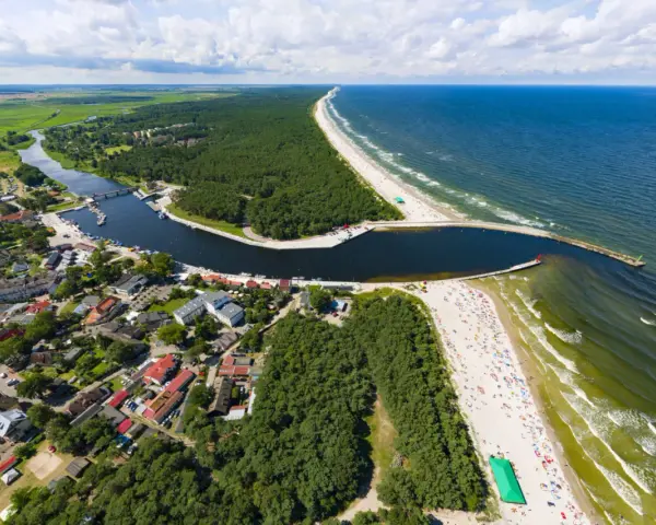 Widok z lotu ptaka na miasteczko nad zatoką, las i plażę. Na falochronie widać czerwoną latarnię morską kikut.
