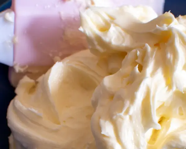 Puszysty, prosty krem z mascarpone bez śmietany, idealny do deserów. Widać go na niebieskim tle, obok różowej łopatki.