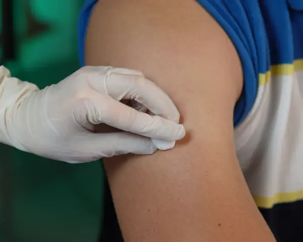 Ręka w rękawiczce dezynfekuje ramię przed podaniem zastrzyku. To przygotowanie do iniekcji śródskórnej.
