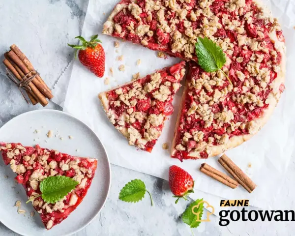 Pyszna tarta z truskawkami i kruszonką, udekorowana miętą, obok laski cynamonu i świeżych truskawek.