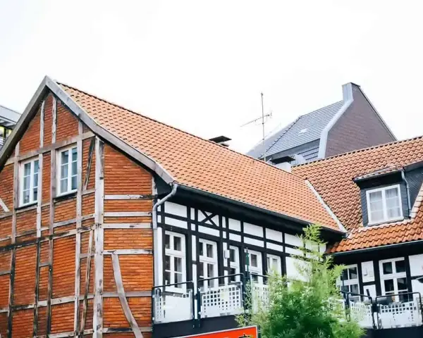 Tradycyjna **konstrukcja muru pruskiego** z ceglanymi wypełnieniami i drewnianymi belkami, obok nowoczesnych budynków.