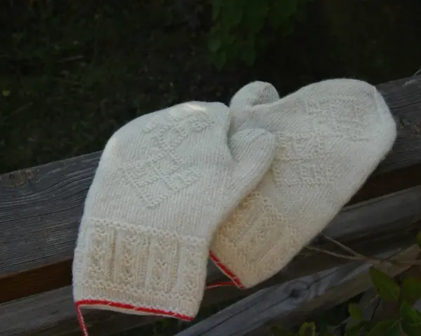 Två par vantar i naturvit ull, stickade med tvåändsstickning och fina mönster. De har en röd kant nertill.