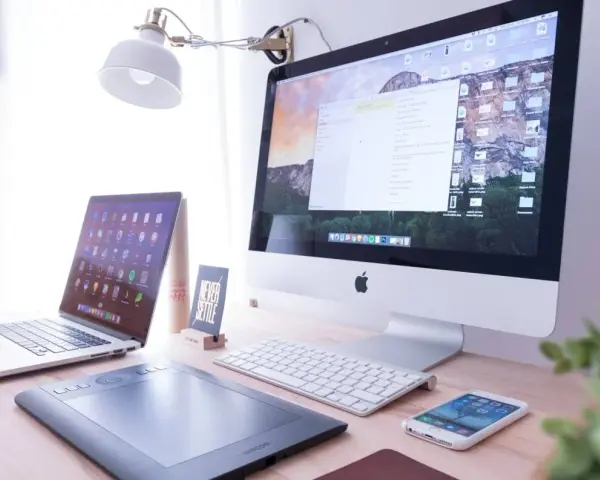 Biurko z iMac, laptopem, tabletem graficznym i telefonem. Na ekranie komputera widać okno programu Adobe Dreamweaver, gotowe do pracy nad stroną.