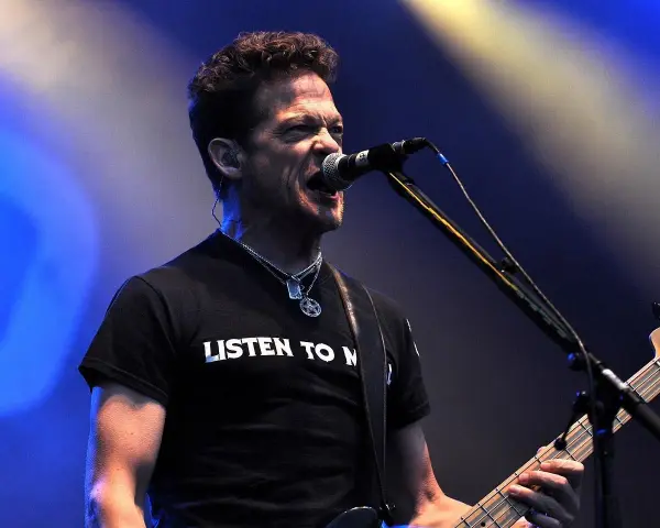 Jason Newsted z zespołu, w czarnej koszulce z napisem "LISTEN TO N", śpiewa do mikrofonu, grając na basie.