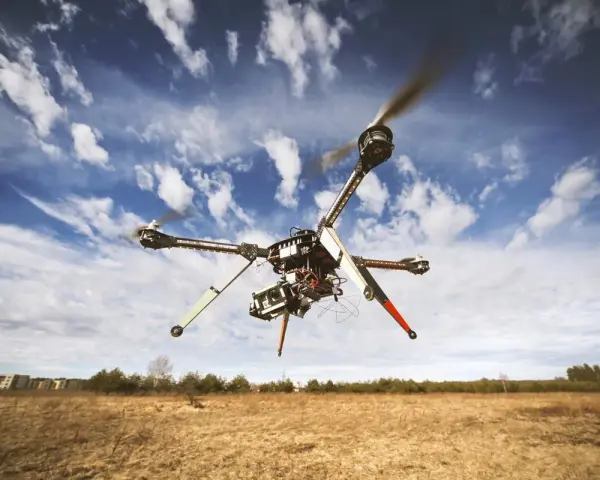 A drone hovers in a blue, cloudy sky over a dry, grassy field, hinting at the need to understand **Montana drone laws** before flying.