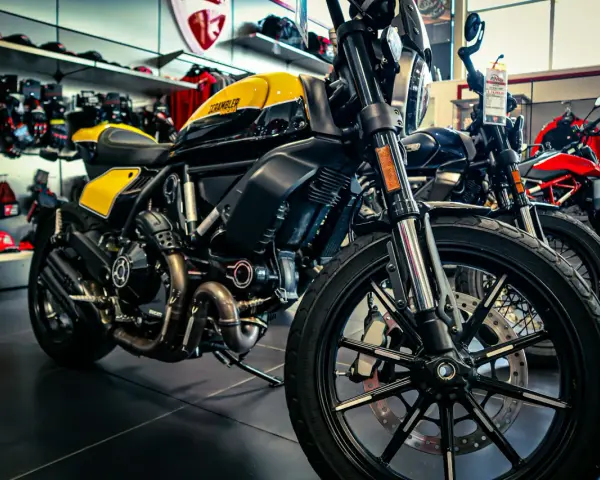 Ducati Scrambler gialla e nera, pronta per i raduni moto. Dietro, altre moto e abbigliamento tecnico.