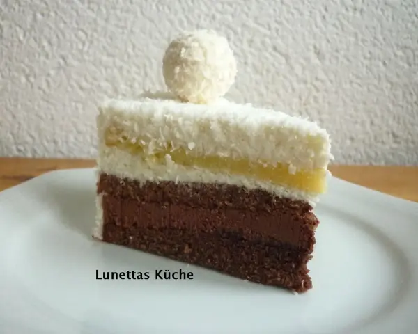 Ein Stück Schoko Kokos Torte mit Kokosraspeln und einer Praline obendrauf.