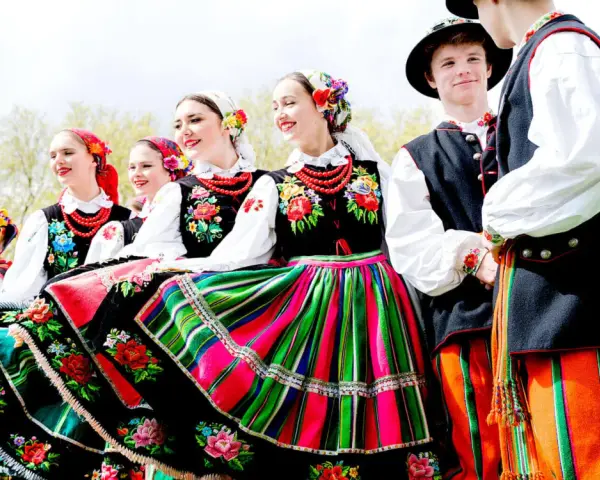 Młodzi ludzie w barwnych strojach ludowych, gotowi do wykonania polskich tańców narodowych.