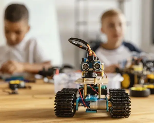 Dzieci budują roboty, ucząc się programowania i inżynierii. W centrum mały robot z czujnikami, w tle chłopcy pracujący nad projektami.