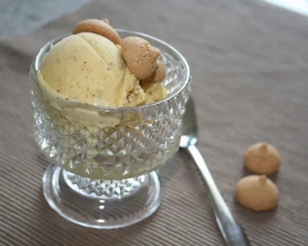Ein Glas mit cremigem Marzipan Eis, garniert mit kleinen Keksen. Daneben liegen zwei weitere Kekse und ein Löffel.