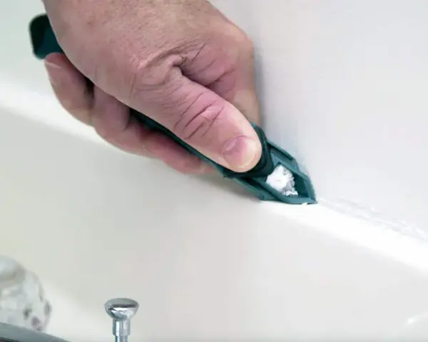 A hand uses a tool to smooth fresh caulk along a bathtub seam, demonstrating how to caulk for a clean finish.