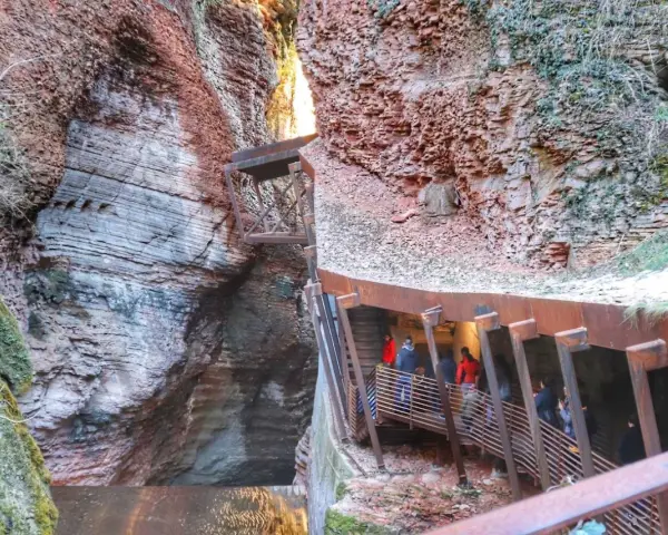 Un orrido ponte alto attraversa una gola rocciosa, con persone che salgono una scalinata metallica.
