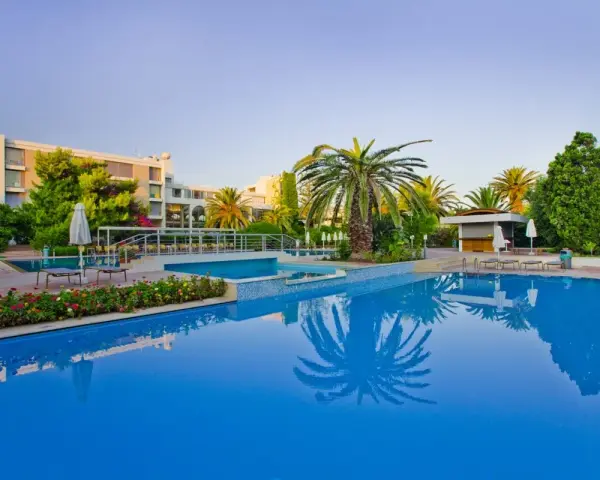Basen hotelowy z palmami i kwitnącymi kwiatami, idealne miejsce na relaks przy Caravia Beach Kos.
