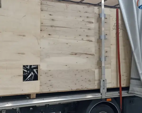 Drewniana skrzynia z widocznym fragmentem felgi, gotowa do transportu. Widać logo firmy transportowej i oznaczenia towaru.
