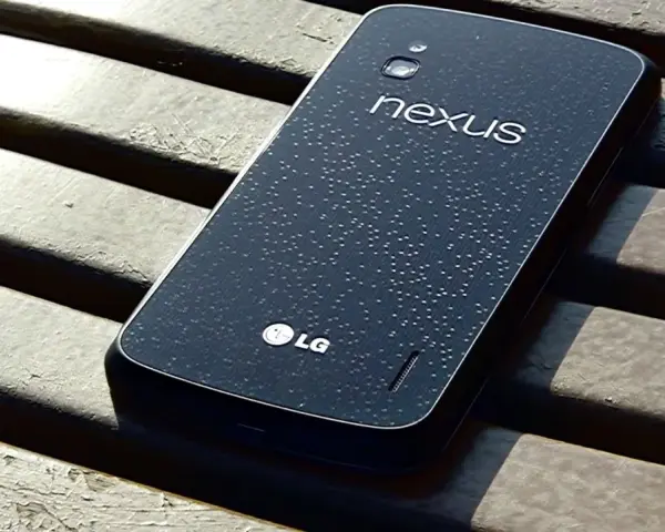 Ciemny tył telefonu LG Nexus 4 z kroplami wody na powierzchni, leżący na drewnianej ławce.