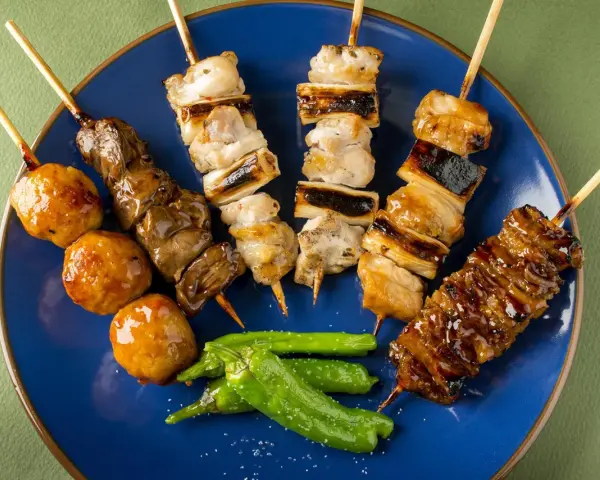 Różnorodne szaszłyki yakitori: kurczak, wątróbka, klopsiki i papryczki shishito, polane sosem.