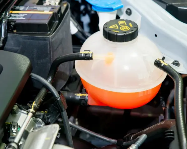 A car's coolant reservoir, showing the orange fluid level. This helps determine how much coolant does a car take.