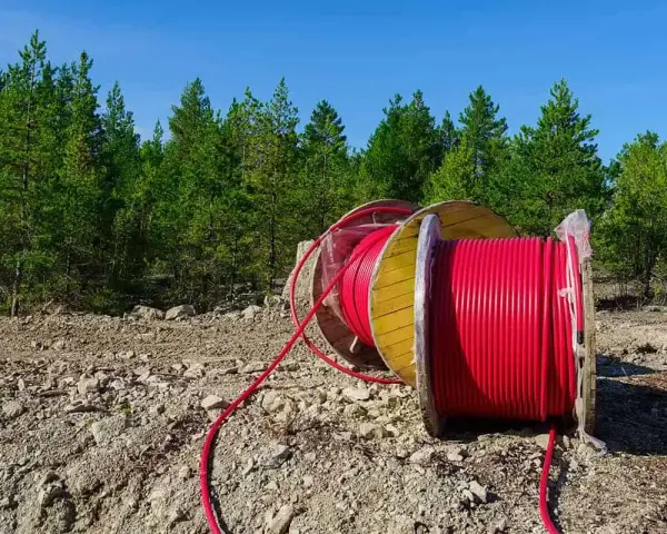 Czerwony kabel na drewnianym bębnie, przygotowany do uzbrojenia działki. W tle las i błękitne niebo.