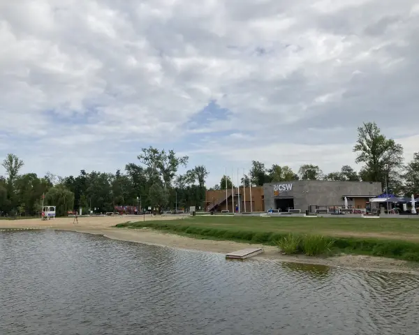Spokojne jezioro małe żnińskie z piaszczystą plażą, budynkiem CSW i zielenią w tle.