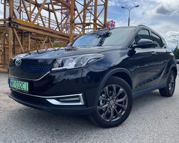 Czarny, lśniący SUV, jeden z chińskich samochodów elektrycznych, zaparkowany obok żółtej konstrukcji budowlanej.