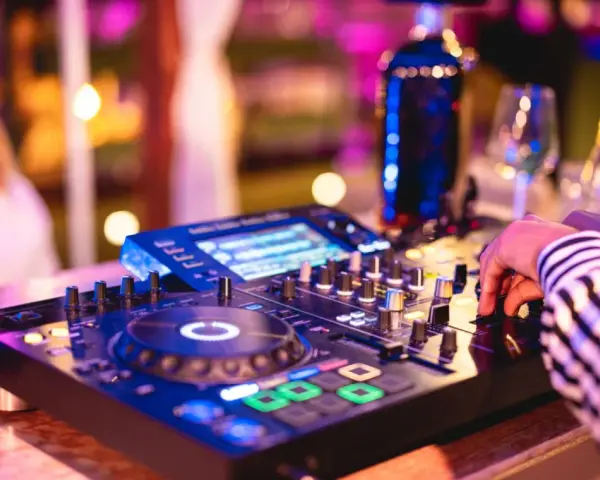 Main d'un dj house connu manipulant la console, lumières vives et ambiance festive.