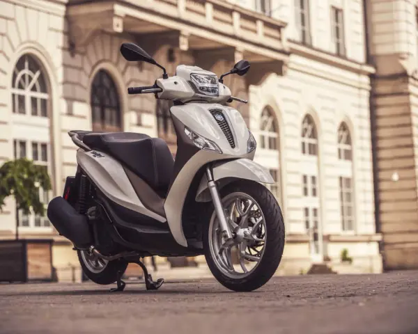 Biały skuter Piaggio Medley zaparkowany na bruku przed zabytkową kamienicą.