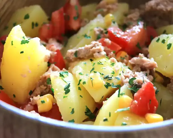 Salade de pommes de terre, thon, tomates et maïs, parsemée de persil frais. Un plat simple et savoureux.