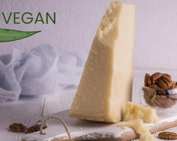 Kawałek sera parmezan, orzechy pekan w szklanej miseczce i liść z napisem FORVEGAN.