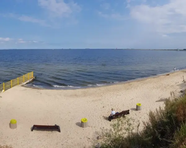 Piękna, piaszczysta plaża dla psów z łagodnym zejściem do morza. W oddali widać falochron i statki.