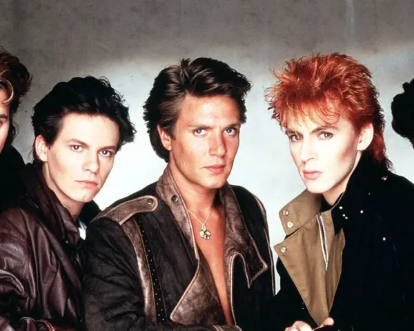 Fünf Männer mit auffälligen Frisuren und 80er-Jahre-Mode, die an ikonische Musikvideos dieser Ära erinnern.
