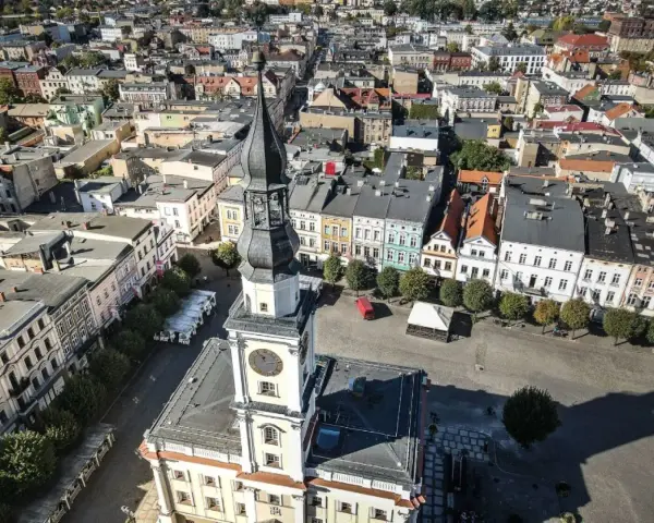 Widok z lotu ptaka na rynek w Lesznie. Wieża ratusza góruje nad kolorowymi kamienicami, ukazując urokliwe leszno atrakcje.