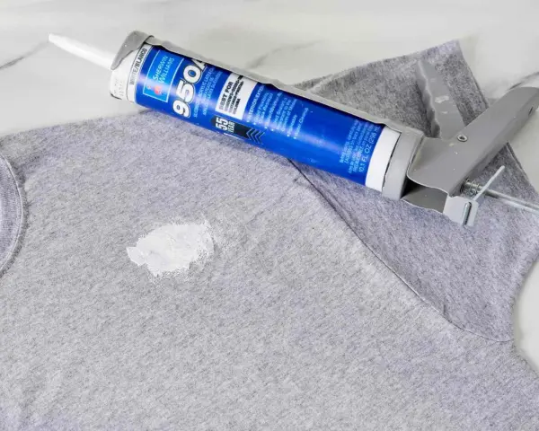 Zaschnięty silikon na szarym T-shircie i pistolet do jego aplikacji. Dowiedz się, jak usunąć zaschnięty silikon z ubrania.