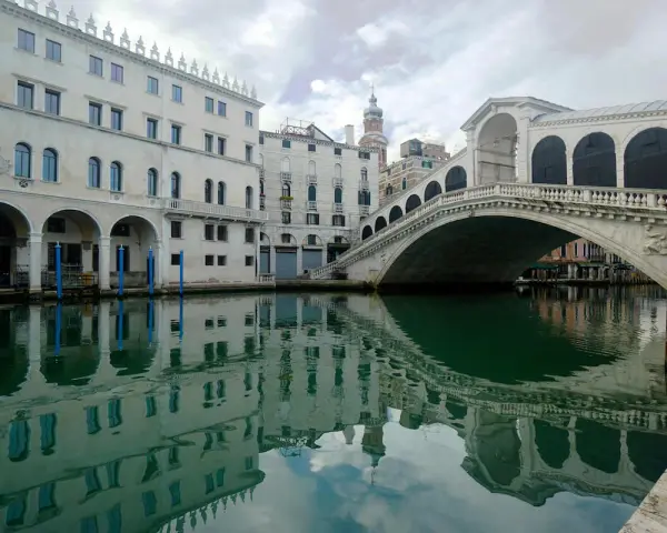 Le vie di Venezia, con il Ponte di Rialto che si specchia sull'acqua verde e gli edifici storici che creano un'atmosfera magica.