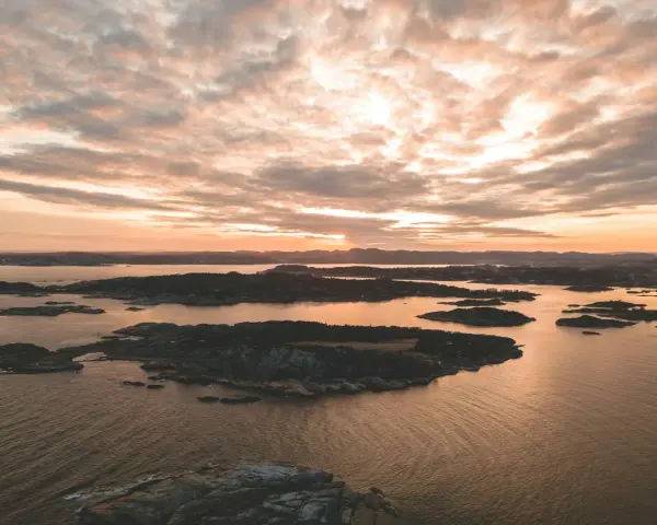 Zachód słońca nad archipelagiem, przypominającym szwedzkie fiordy. Woda odbija złote światło, a chmury malują niebo.