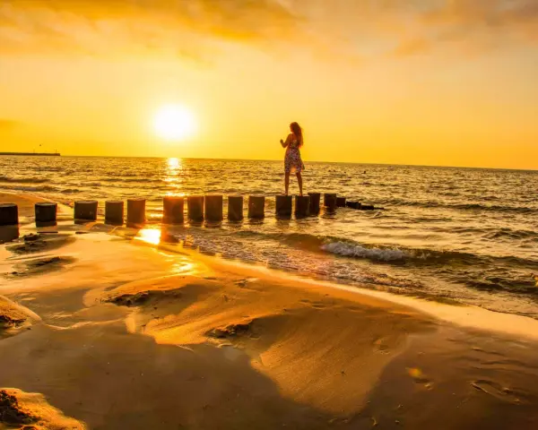 Zachód słońca na plaży w Ustce. Dziewczyna w kwiecistej sukience stoi na falochronie, ciesząc się złotą godziną.