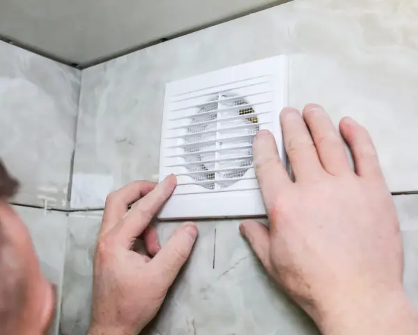 Installation d'un nouveau ventilateur pour la **salle de bain ventilation**. Mains ajustant l'appareil blanc sur un mur carrelé.