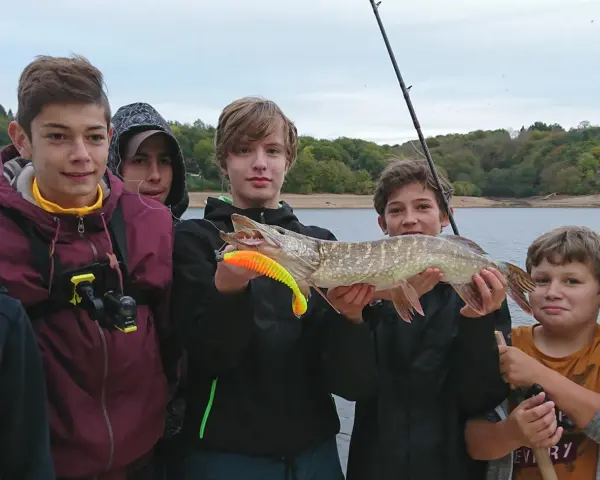 Des jeunes pêcheurs fiers de leur prise lors d'une colonie de vacances pêche. Un beau brochet exhibé devant un lac.