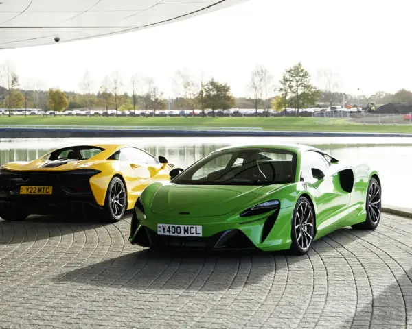 Dwa sportowe samochody McLaren Artura: jeden zielony z przodu, drugi żółty z tyłu, stojące na zewnątrz.