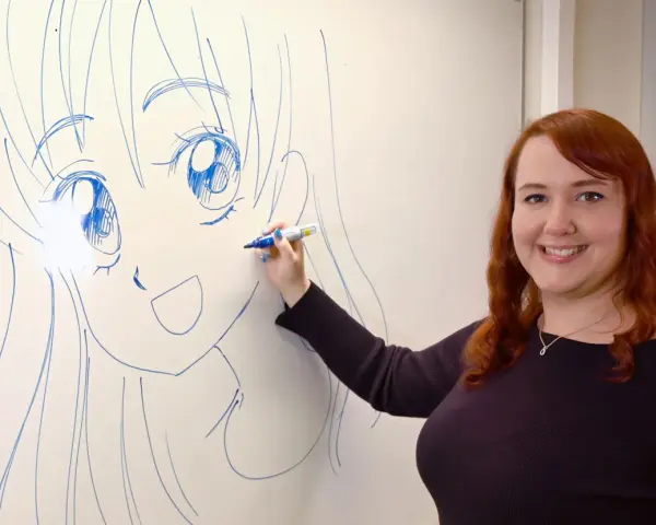 En kvinna med rött hår ritar en stor manga teckning på en whiteboard.