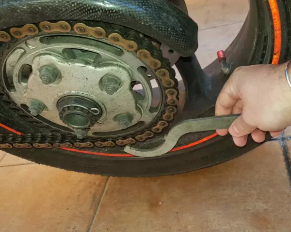 Mano con chiave speciale per regolare la catena della moto, mostrando come tirare la catena.