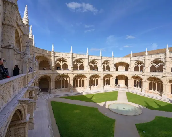 The Jerónimos Monastery, a stunning monastery in Portugal, features a grand courtyard with intricate stonework and a lush green lawn.